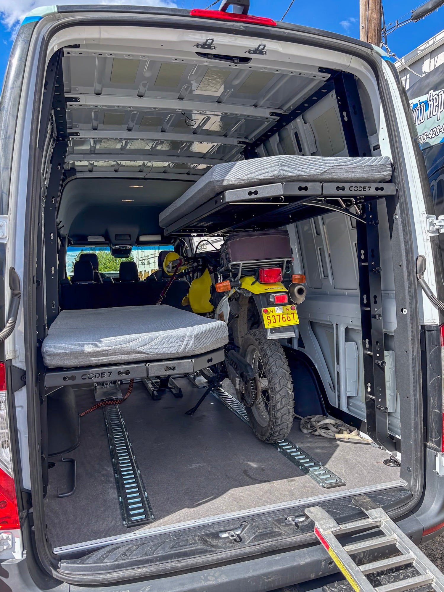 170" Sprinter van interior with a bunk bed setup and motorcycle inside, under a clear blue sky.